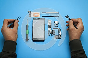 Man repairing broken smartphone on light blue background, above view
