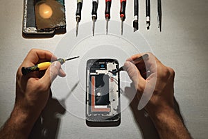 Man repairing broken smartphone at light grey table, top view