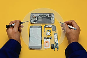 Man repairing broken smartphone on yellow background, above view