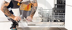 man repairing dishwasher. Male hand with screwdriver installs kitchen appliances, close up