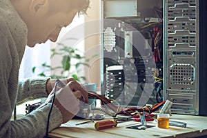 Man repairman is trying to fix using the tools on the computer that is on a workplace in the office