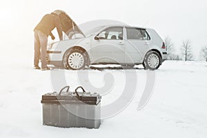 A man repairs a car in winter on snow in the background is a discharged battery, copy space photo