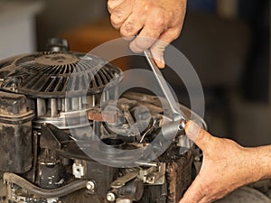 A man repairs the engine of a gasoline lawn mower. hands holding wrench