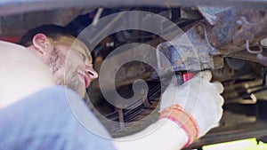 Man repairs an old car, changes shock absorbers, close-up, guy lies under a truck