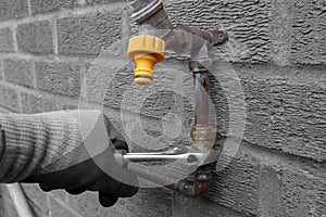 Man replacing burst copper water pipe outdoors. Unscrewing a brass connector with a spanner wrench.