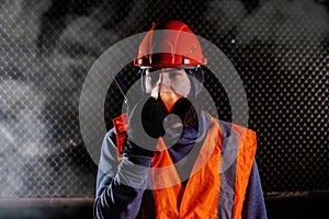 Man in respirator talking on walkie-talkie during fire in industrial building
