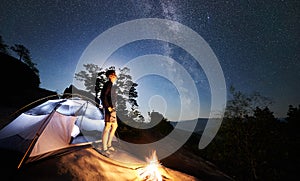 Man resting beside camp, bonfire and tourist tent at night