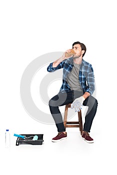man resting on chair and drinking coffee near roller tray and paint roller