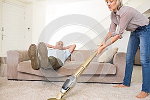 Man resting on couch while woman vacuuming area rug