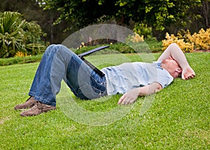 Man resting on lawn with half closed laptop