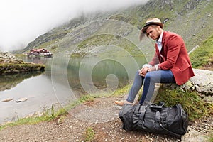 Man is resting near a mountain lake with cabin