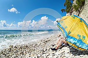 Man resting on rocky beach under umbrella