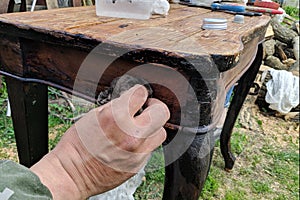 A man restores old furniture in the fresh air. Removes old paint from a vintage table.