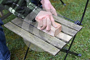 Man restoring a wooden garden chair, sanding and cleaning the weathered wood, removing algae and moss to refresh the outdoor