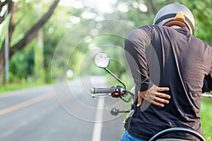 Man rider touching on his back side and feeling tired after long ride motorcycle. Outdoor shooting on the road with copy space