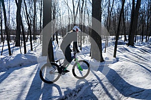 A man rides a bicycle on a pump-track in the winter in a helmet.