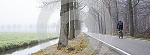 man rides bike on country road on misty winter morning in the netherlands near utrecht