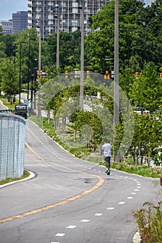 Man rides electric personal mobility scooter down winding running-bike trail with wildflowers and lush vegetation around and the