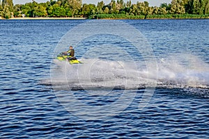 A man rides a PWC on the Dnieper River in Kherson, Ukraine - back view. White foam, splashes and trail created by a jet ski on the