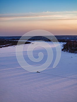 A man rides a snowmobile on a frozen snow-covered river at sunset in winter. view from above.