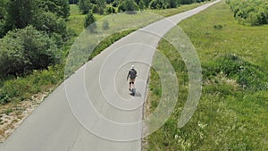 Man rides at straight road on longboard at sunset time aerial 4k. The guy rides a longboard on the way to the field, the