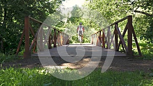 A man is riding a bicycle across the bridge in the park. slow motion