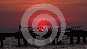 A man riding a bicycle across a bridge at sunset.