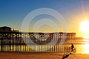 Man riding bicycle along beachfront during a Pacific Ocean sunset in San Diego