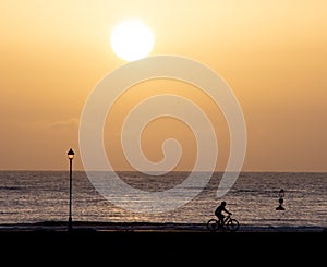 Man riding bicycle on beach path at sunrise