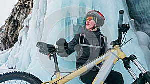 Man is riding bicycle near ice grotto. Rock with ice caves icicl