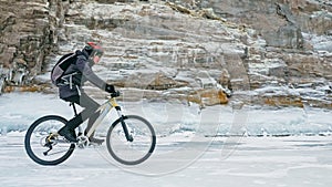 Man is riding bicycle near ice grotto. Rock with ice caves icicl