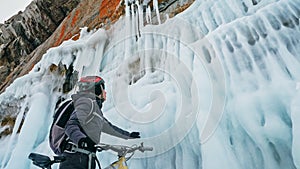 Man is riding bicycle near ice grotto. Rock with ice caves icicl