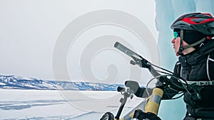 Man is riding bicycle near ice grotto. Rock with ice caves icicl