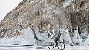 Man is riding bicycle near the ice grotto. The rock with ice caves and icicles is very beautiful. The cyclist is dressed