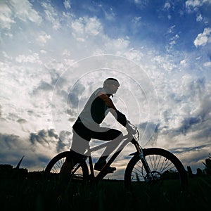 Man riding bicycle over sunset sky background