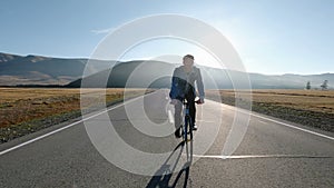 Man riding a bike on asphalt road towards the sunny sunset sky 20s 4k.