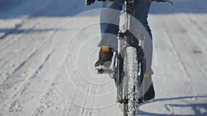 Man riding bike on a snowy day, slippery road conditions. Close up of man feet pedaling. Bicycle wheels in snow. Courier