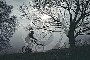 Man riding a bike uphill through foggy autumn morning