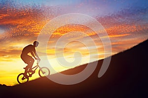 Man riding a bmx bike uphill against sunset sky. Strength, challenge.