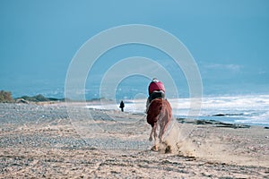 Man riding on a brown galloping horse along Ayia Erini beach against a rough sea