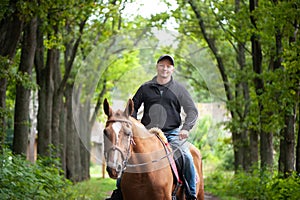 Man riding a horse in a beautiful forest, smiling, looking at the camera