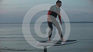 Man riding on a hydrofoil surfboard on large blue lake at the pink sunset