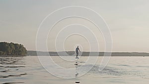 Man riding on a hydrofoil surfboard on large lake at golden sunset