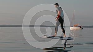Man riding on a hydrofoil surfboard on large lake at golden sunset