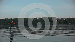 Man riding a hydrofoil surfboard on large lake at golden sunset sitting on knees