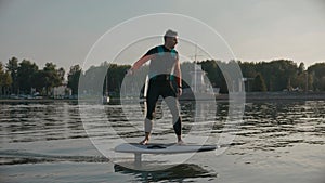 Man riding on a hydrofoil surfboard on large lake at warm sunset