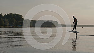 Man riding on a hydrofoil surfboard on large lake at warm sunset