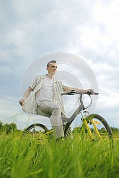 The man is riding a mountain bike. A fashionable guy came to nature in the field. The guy on the background of nebt. Bright yellow