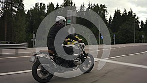 Man riding scrambler motorbike on the highway through the autumn forest