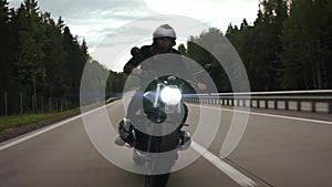 Man riding scrambler motorbike on the highway through the forest, front view